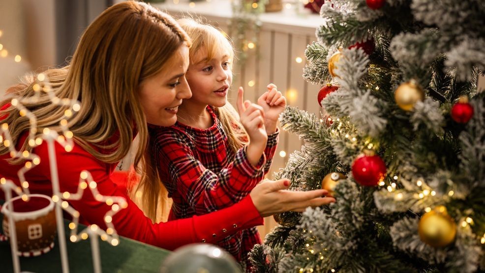 Mother and daughter decorating Christmas tree, eating cookies and drinking tea.