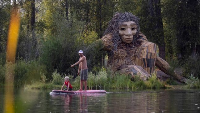 JACKSON HOLE, WY - JULY 26: A father and son paddle past "Mama Mimi," a wooden sculpture created by Danish artist Thomas Dambo in Rendezvous Park on July 26, 2021 in Jackson Hole, Wyoming. Dambo's public art, featuring troll figures are made from recycled and found materials. This troll was completed in June 2021 and joins other public art works made by Dambo throughout the world in places like Puerto Rico, China, Australia, and more. (Photo by Natalie Behring/Getty Images)